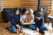 © Tomsickova - Mother and her three children in a little fancy wooden cottage, reading a book, drinking tea