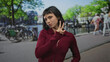 © Krakenimages.com - Young hispanic woman wearing red cardigan and gold earrings makes peace sign with hand in amsterdam street; playfulness.