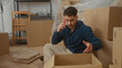 © Krakenimages.com - Young hispanic man in new home surrounded by boxes talking on phone in living room apartment interior unpacking