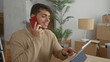 © Krakenimages.com - Man holds phone while talking at home as hispanic young resident sorts boxes next to tablet and mobile charger in an empty house.