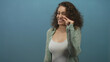 © Krakenimages.com - Woman pinching nose with thumb and forefinger, wearing white tank top and sheer green shirt, posed in studio against blue wall; disgust.