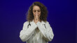 © Krakenimages.com - Young hispanic woman doctor wearing white coat and stethoscope, pressing hands together with closed eyes in blue studio setting; calm compassion.
