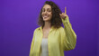 © Krakenimages.com - Woman points finger up in studio against purple wall, young hispanic smiling in yellow shirt and white tank; confidence optimism.