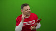 © Krakenimages.com - Young man in a red volunteer shirt listens and writes on a clipboard against a green wall, focusing attentively.