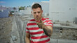 © Krakenimages.com - Young man with tattoo in striped shirt gestures at camera in construction site, showcasing modern urban setting with bold expression.