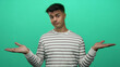 © Krakenimages.com - Young man in striped shirt gestures over isolated green background, looking puzzled and confident, expressing indifference and calm, conveying a relaxed mood.