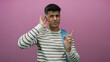 © Krakenimages.com - Young man gestures confusion over pink background, wearing striped sweater and backpack, expressing curiosity and listening.
