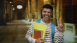 © Krakenimages.com - Young man smiling indoors at a museum holding notebooks showing peace sign wearing a striped shirt and blue backpack in an artistic historical setting