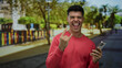 © Krakenimages.com - Young man in a city street smiling with a smartphone making a victory horn gesture against a colorful urban background