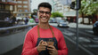 © Krakenimages.com - Young man wearing glasses in a red sweater holding a coffee cup and smiling outdoors on a busy city street.