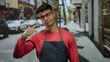 © Krakenimages.com - Young man in apron and glasses pointing down on city street with blurred background showcasing vibrant urban setting.