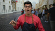 © Krakenimages.com - Young man wearing glasses and apron holds scissors while standing on a bustling city street, showcasing his barber skills in an energetic urban environment.
