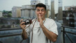 © Krakenimages.com - Young man with camera smiles playfully on a city street, capturing urban moments with joy and creativity against a scenic backdrop.