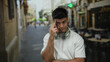 © Krakenimages.com - Young man with headphones gestures on a city street terrace with blurred cafe in background, wearing white shirt, illustrating urban lifestyle and diverse emotions.