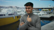© Krakenimages.com - Young man with glasses gestures no at seaside port with boats in background, wearing grey turtleneck, looks confident outdoors, expressing disapproval with finger pointing up.