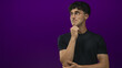 © Krakenimages.com - Young hispanic man wearing glasses and a black t shirt, hand on chin pensive pose in purple studio with slight smile and relaxed posture; thoughtful.