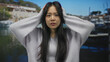 © Krakenimages.com - Woman with long dark hair at seaside beach, expressing emotion with hands on head and wearing casual sweater outdoors against a peaceful waterfront backdrop.