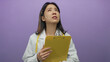 © Krakenimages.com - Young chinese woman doctor in uniform with stethoscope and clipboard looks puzzled against isolated purple background.