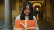 © Krakenimages.com - Woman smiling with a gift outdoors at an old university campus with columns and arches in the background.