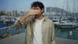 © Krakenimages.com - Hispanic man covers face at sunny port with boats and mountain backdrop, wearing plaid shirt, evoking travel and introspection in a nautical setting.