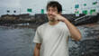 © Krakenimages.com - Man smiling on a rocky beach touching his nose while wearing a white shirt with ocean and buildings in the background under cloudy sky showing a relaxed vacation setting.