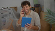© Krakenimages.com - Hispanic man using tablet and mobile phone in modern new home surrounded by moving boxes indicating a recent move into the house.