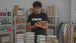 © Krakenimages.com - Hispanic man volunteering in donation center organizing food supplies wearing volunteer shirt surrounded by packaged meals clothing donations and shelves.