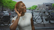 © Krakenimages.com - Woman cupping ear with hand on a canal street by river lined with bicycles, listening attentively; curiosity.