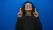 © Krakenimages.com - Woman smiling and pointing upwards against a vivid blue background, showcasing middle age with a joyful expression.