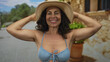 © Krakenimages.com - Hispanic woman in bikini and hat enjoys a sunny day on a street in an old town, radiating joy and relaxation outdoors.