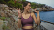 © Krakenimages.com - Woman holding 1kg dumbbell and flashing peace sign with bare stomach at coast wooden railing; joy fitness.