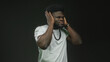 © Krakenimages.com - Man covering ears with both hands, wearing white t shirt and beaded necklace in studio against dark wall; annoyance.