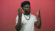 © Krakenimages.com - Young african american man with hands raised and open palms, wearing beaded necklace and white tee against pink studio wall; surprise questioning.