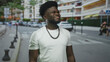 © Krakenimages.com - Young black man smiling and looking up on a busy city street wearing a white t shirt and beaded necklace; confidence optimism hope.