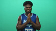© Krakenimages.com - Young man clapping hands in studio wearing blue basketball jersey number 77, smiling toward camera against green wall; celebration.