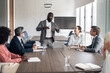© Jelena - Black businessman leading a diverse team meeting in boardroom