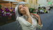 © Krakenimages.com - Senior woman with gray hair covers nose from bad smell on a busy street terrace outside a restaurant, surrounded by blurred people and vivid flowers.