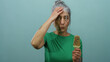 © Krakenimages.com - Elderly woman with grey hair in a green shirt holding an ice cream bar against a blue background, looking expressive and isolated with a surprised demeanor.