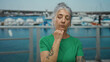 © Krakenimages.com - Woman with grey hair in green shirt standing thoughtfully by a seaside port with boats, captured outdoors exhibiting tattoos and serene expression.