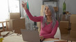 © Krakenimages.com - Senior woman with grey hair sits in a new home surrounded by boxes, using a laptop and pointing thoughtfully while unpacking in a cozy apartment living room.