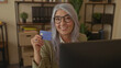 © Krakenimages.com - Woman smiling in an office holding a blue credit card, showcasing senior professional lifestyle with a confident expression and grey hair in work environment