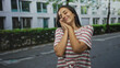© Krakenimages.com - Woman pressing hands to cheek with closed eyes on an urban street near building, striped knotted tshirt, relaxed pose and subtle smile; serenity daydreaming.