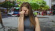 © Krakenimages.com - Woman in blue sleeveless top pinches nose on busy street lined with trees and parked cars; disgust.