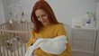 © Krakenimages.com - Woman holding baby in cozy bedroom, wearing yellow sweater, surrounded by white decor, nurturing infant in peaceful home setting with crib and baby products in the background.