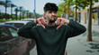 © Krakenimages.com - Young man with a beard and curly hair gives a double thumbs-down on an urban street lined with cars and trees, expressing disapproval in a city setting.