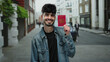 © Krakenimages.com - Man smiling holding british passport on urban street in city, showcasing travel and identity outdoors on a bright day.