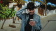 © Krakenimages.com - Young man smiling on urban street holding smartphone in casual denim jacket with vibrant greenery backdrop and clear sky, embodying modern city life and outdoor leisure.