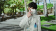 © Krakenimages.com - Young man wearing mask in white coat standing in park outdoor with blurred green background during daytime, pointing at face mask with pens in pocket.