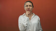 © Krakenimages.com - Middle aged blonde woman resting chin on hand in studio framed by vibrant orange backdrop; quiet introspection doubt.