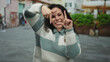 © Krakenimages.com - Young woman posing playfully on city street wearing glasses and striped sweater, creating frame with fingers during daytime, showing joyful expression in urban setting.